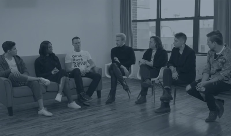 Seven people sit in chairs for a panel discussion in a large city studio